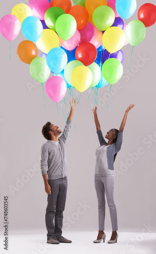 Happy couple, party and celebration with balloons for event, birthday or romance on a gray studio background. Excited man and woman with colorful blowups of helium for date, giveaway or anniversary photo