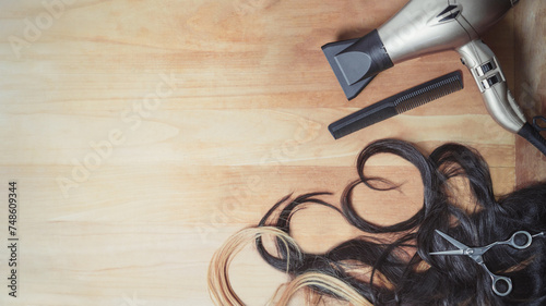 Hairdresser tools and piece of wavy dark hair and blonde hair with copy space on the wooden background. Heart shape.