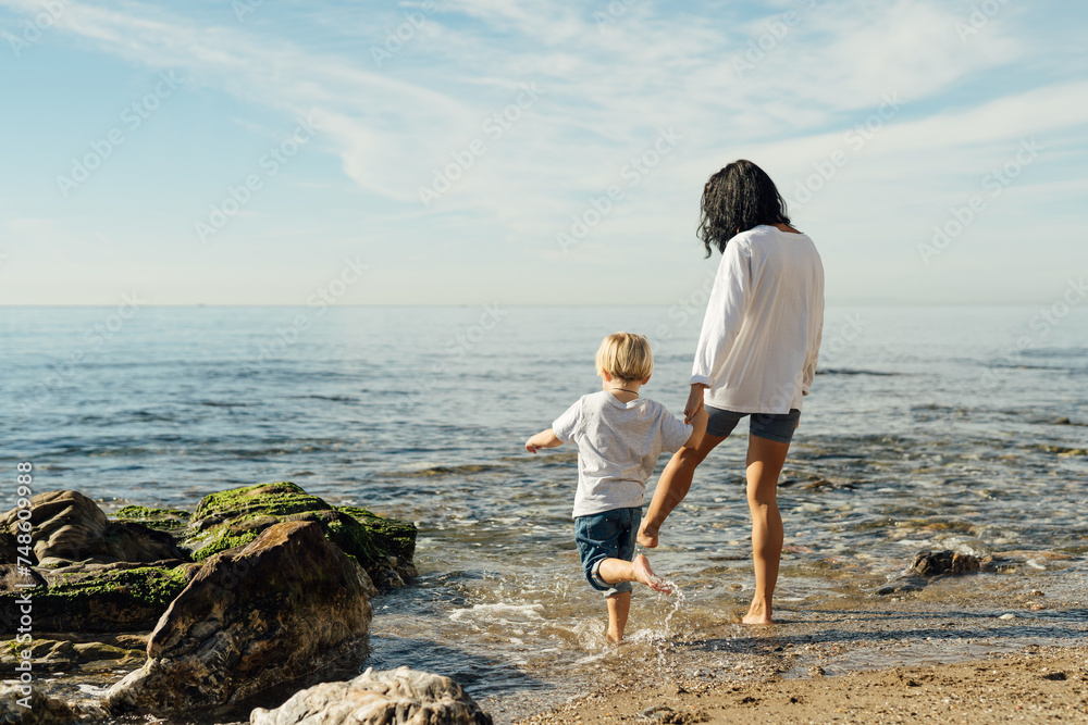 mother and son go into the sea. mother and son test the water with bare feet. mother and son having fun on the seashore. Mum and toddler family time