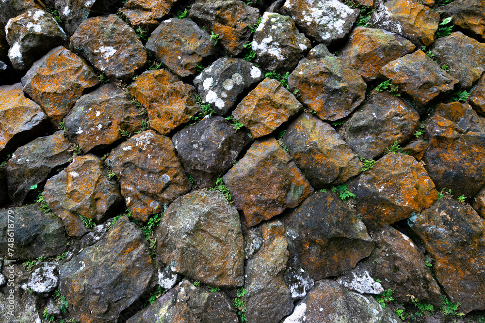 Old stone wall with many rust spot on it, and some green plants living in between, in Jinguashi, New Taipei City, Taiwan.