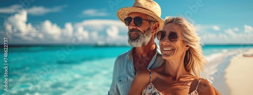 Happy beautiful mature couple relaxing on the beach near the ocean. Couple enjoying life and leisure at resort, related to travel, romance, beach vacations, and relaxation