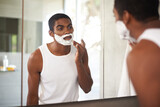 Black man, mirror and shaving cream on face in bathroom for grooming, skincare or morning routine. Reflection, beard and person apply foam for cleaning, health and hair removal for hygiene in home