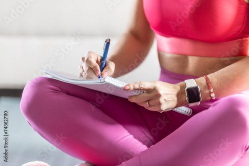 Sporty woman sits on a mat and writes down future training plans for achieving sports results
