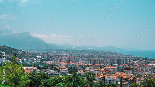 The photo captures the cityscape of Alanya, with the majestic backdrop of a towering mountain, harmonizing urban life with the grandeur of nature's presence, offering a picturesque view of the city's 