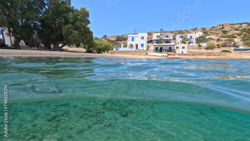 Underwater split photo of paradise crystal clear sea beach of Agios Georgios in main port of Irakleia island covered in Armirikia trees providing natural shade, small Cyclades, Greece
