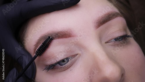 A close-up of a girl's eyebrows after permanent makeup procedure, a master brushes eyebrow hairs with a brush. Permanent makeup procedure, performing PMU of eyebrows