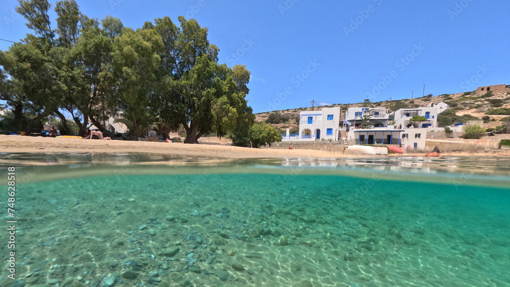Obraz premium Underwater split photo of paradise crystal clear sea beach of Agios Georgios in main port of Irakleia island covered in Armirikia trees providing natural shade, small Cyclades, Greece
