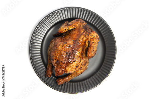 A whole delicious roasted chicken seasoned with herbs in a black plate top view isolated on white background clipping path