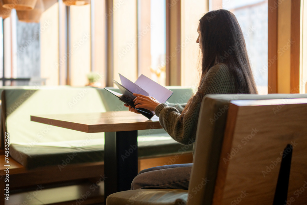 Young Woman Seated on a Green Sofa Choosing a Meal From a Menu in cafe Young Woman Seated on a Green Sofa Choosing a Meal From a Menu in cafe