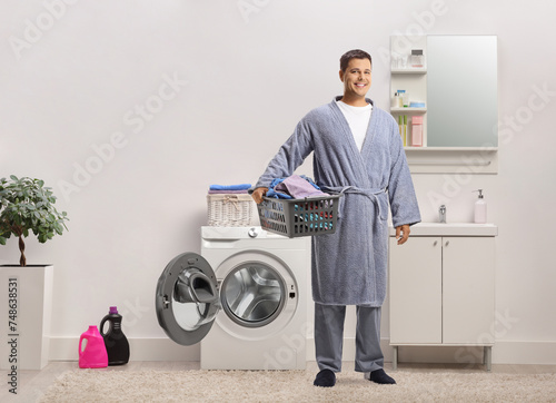 Young man in a bathrobe holding a laundry basket in a bathroom