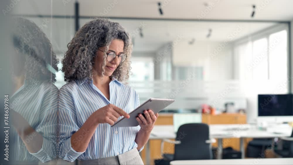 Middle aged professional business woman using tab computer in office. Mature busy happy businesswoman bank manager, older female corporate executive holding digital tablet standing at work.