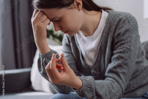 Selective focus of upset worried young woman holding wedding ring think of marriage dissolution or divorce having family problems. Unhappy sad brunette girl stressed with relationships end or breakup photo