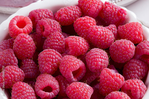 fresh berries. a large number of fresh raspberries lie in a white patterned plate, close-up, berry concept