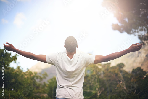 Man, freedom and arms stretched, happiness and appreciate nature in sunlight. Black male person, outdoors and lensflare on vacation for adventure or optimist, grateful and wellness or blue sky