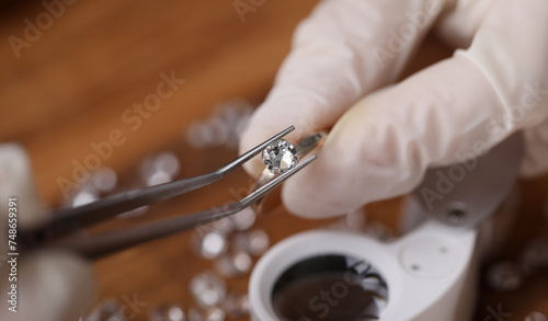 Close-up view of persons hands in protective gloves holding special equipment and examining quality of diamond. Magnifying loupe on table. Luxury jewelry concept