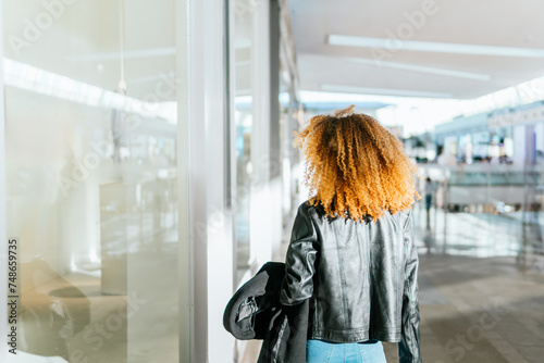 Young black girl with afro hair walks through the shops of a shopping center window shopping. She has her back turned and her face cannot be recognized. photo