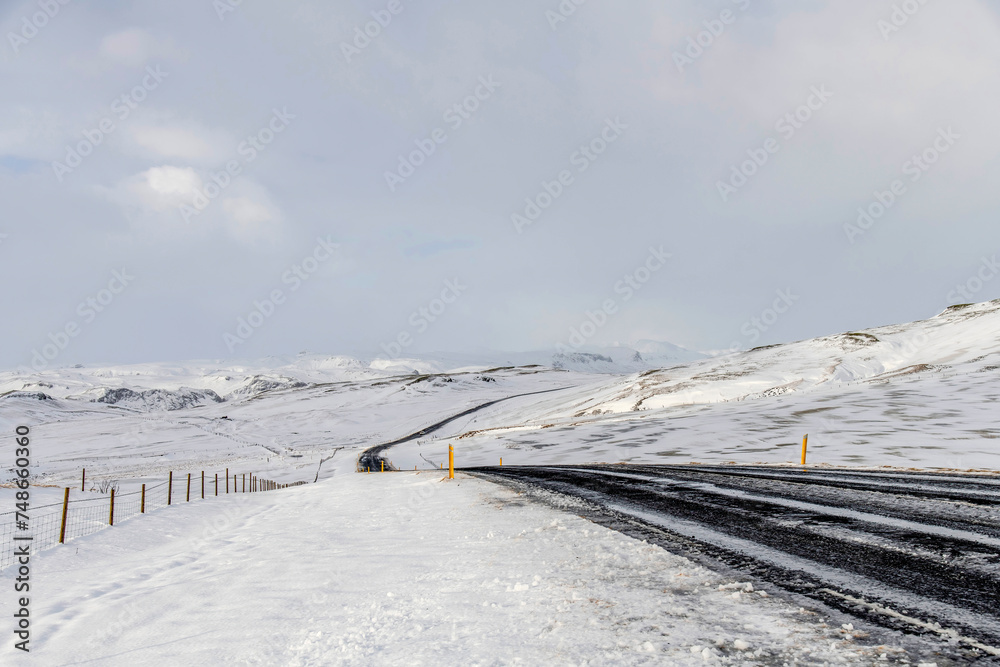 Panoramic low angle winter landscape in Iceland with white clouds over snowy and icy hilly landscape partly cleaned road winding through the landscape Panoramic low angle winter landscape in Iceland with white clouds over snowy and icy hilly landscape partly cleaned road winding through the landscape