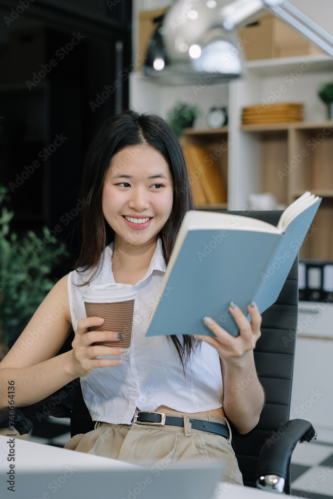 Asian businesswoman sits in a office reading a book at leisure and enjoys a coffee. Asian businesswoman sits in a office reading a book at leisure and enjoys a coffee.