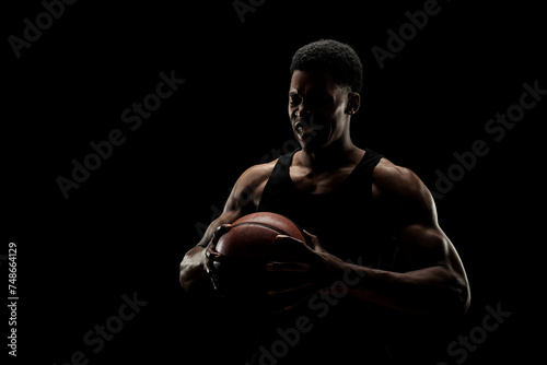 Basketball player holding a ball against black background. Screaming african american man silhouette.