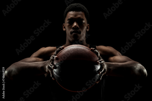 Basketball player holding a ball against black background. Serious concentrated african american man.