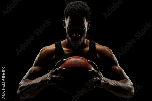 Basketball player holding a ball against black background. Serious concentrated african american man. © Nikola Spasenoski