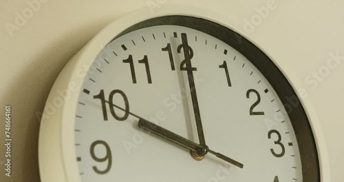 close-up of a white wall clock showing the time 10:00. the seconds hand moves slowly