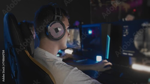 Caucasian teen gamer in headset playing PC video game at computer club. E-sport championship tournament, cyber sport team. Multiplayer online competition tactical first-person shooter photo