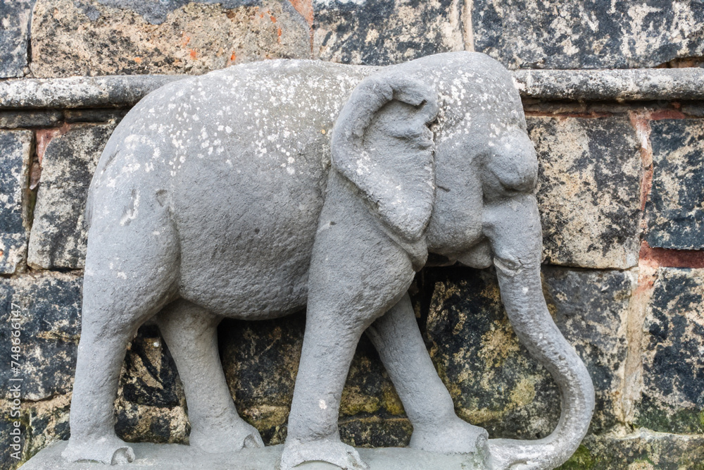 elephant statue A large gray stone elephant stands near a brick wall, side view, close up, art concept