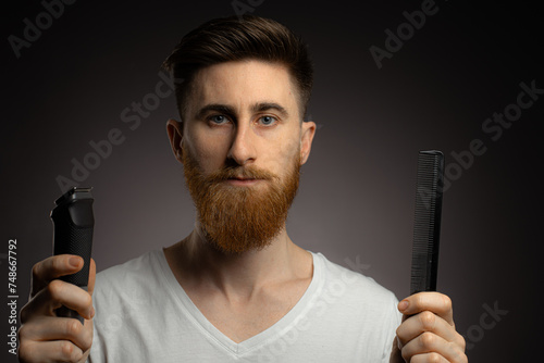 Man shaving whiskers hair by himself, self haircut at home in front of mirror in the bath. Male with long haircut using shaving machine trimmer.