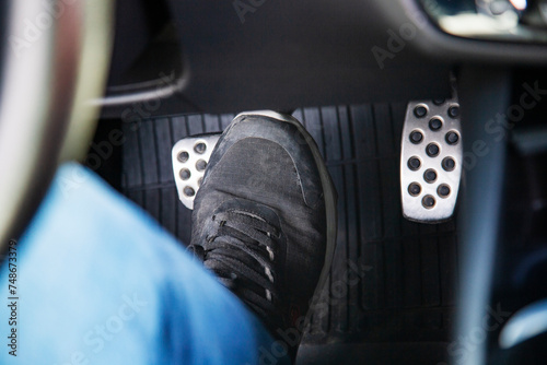 man's feet in black sneakers on the floor in a car pushing down the brake pedal, carefully driving car, waiting on the traffic light concept