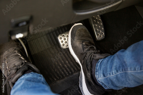 man's feet in black sneakers on the floor in a car pushing down the brake pedal, carefully driving car, waiting on the traffic light concept photo