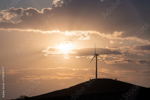Aerogenerador en el horizonte sobre una colina al atardecer. el sol al fondo en un cielo con nubes justo momento antes de ponerse.