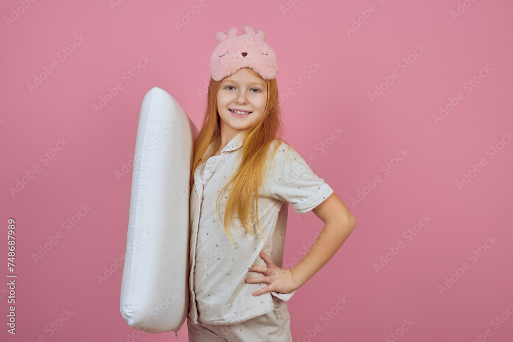 Smiling redhead teen girl holding pillow and wearing sleeping mask on pink background. Smiling redhead teen girl holding pillow and wearing sleeping mask on pink background.