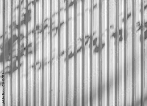 Fondo abstracto con un patrón vertical en una pared metálica con sombras de las hojas de los árboles, en blanco y negro