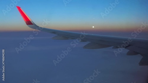 Real time of aircraft wing over fluffy clouds against colorful sundown sky with sun in evening