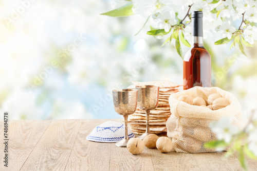 Passover celebration concept. Matzah, red kosher and walnut on wooden vintage table table in front of spring blossom tree garden and flowers landscape with sun rays with copy space. Mock up.