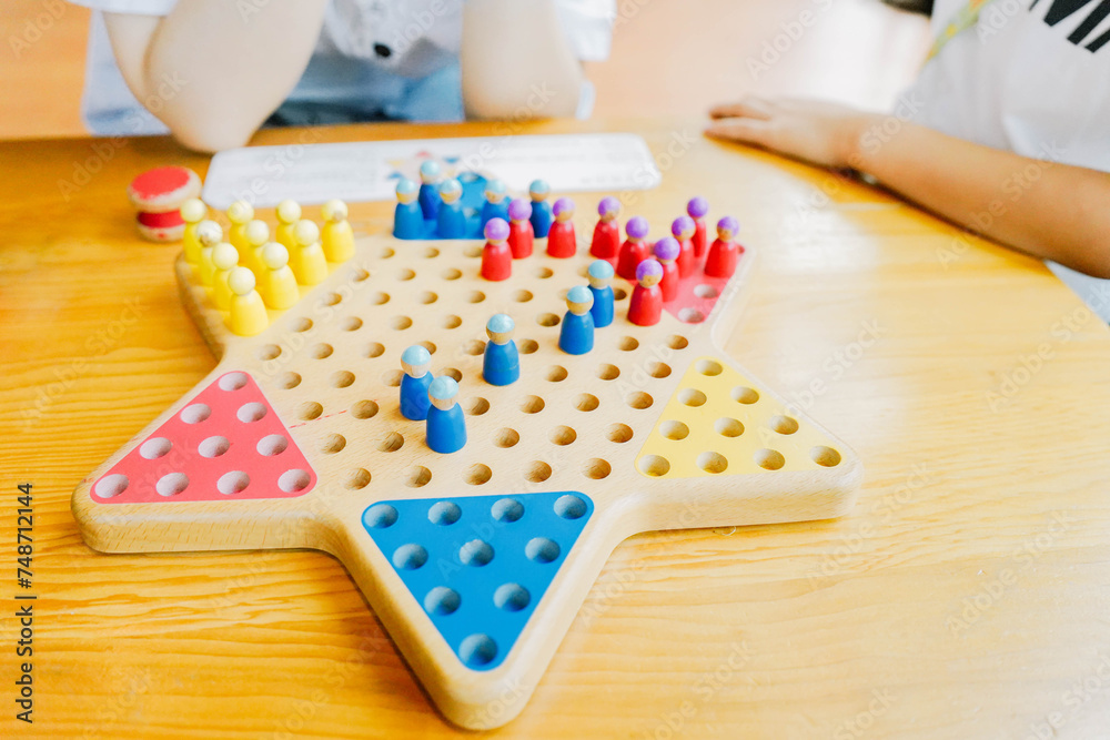 Kids are playing Chinese checkers at a wooden table. Three-player boardgame of Diamond Game (variant of Chinese Checkers , variation of Halma strategy board game) on green baize table.