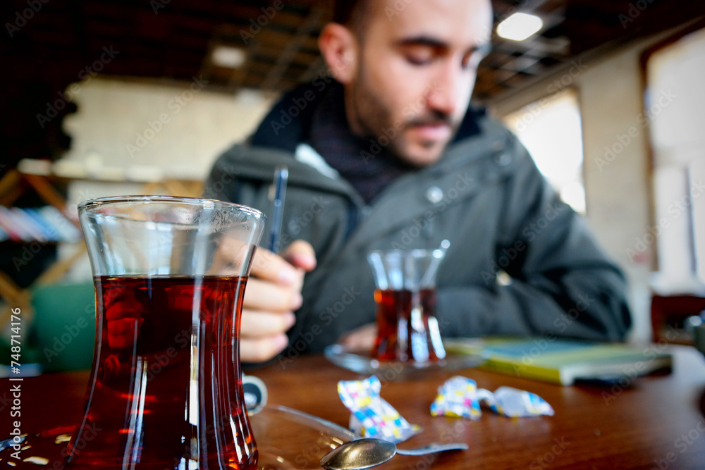 A male student reading a book with tea in a cafe.