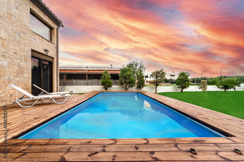 An outdoor swimming pool adjacent to a luxurious villa, captured during the evening hours with a breathtaking sky showcasing stunning colors.