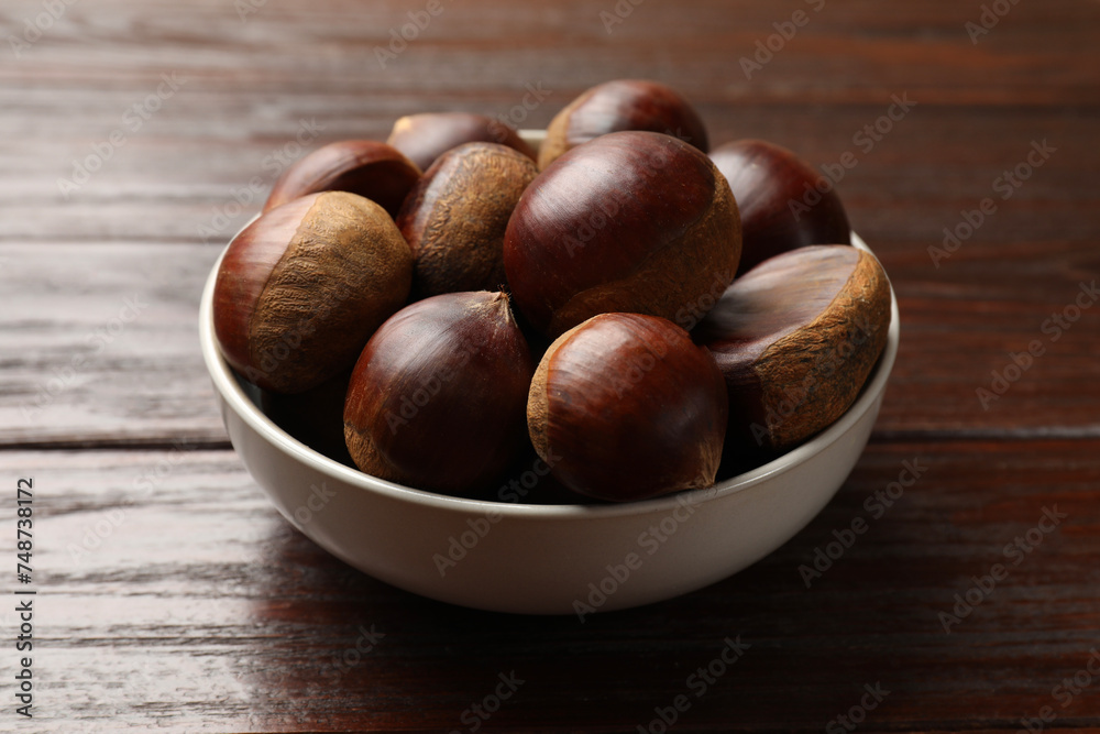 Sweet fresh edible chestnuts in bowl on wooden table, closeup Sweet fresh edible chestnuts in bowl on wooden table, closeup