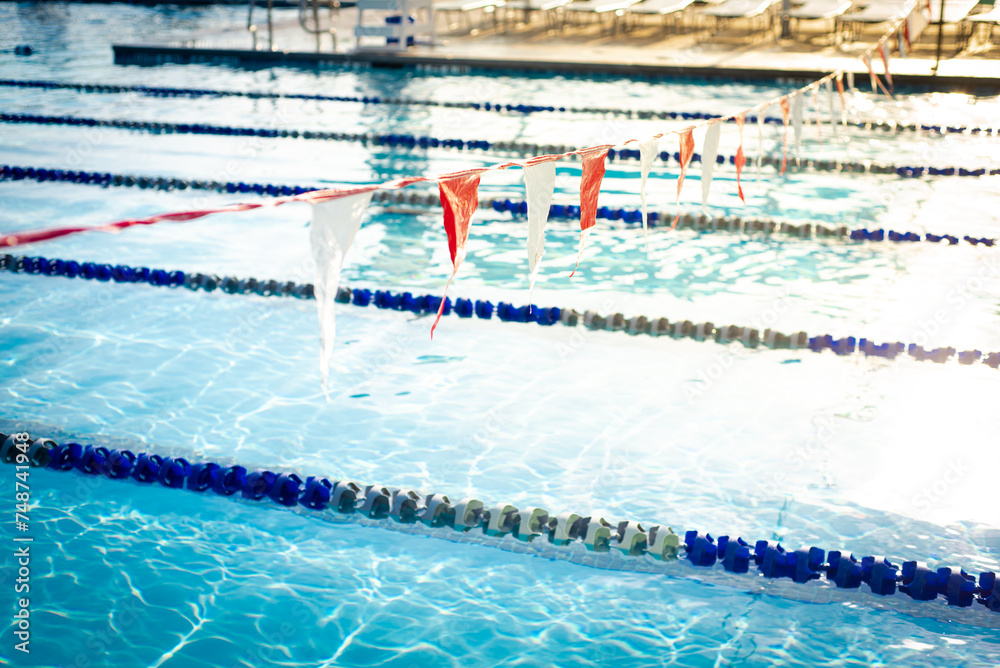 Shallow DOF string of colorful triangular backstroke flags hanging over public competitive swimming pool with pool lane divider rope and floats, clean water no swimmer, Dallas, Texas, healthy