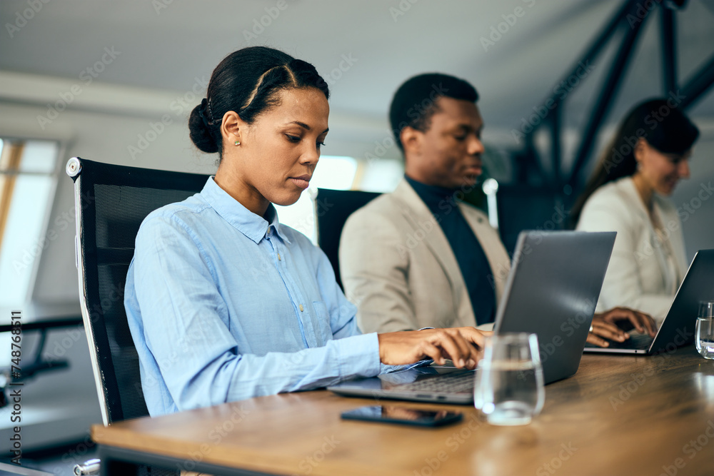 Focus on the businesswoman using her laptop while having a meeting with her colleagues.
