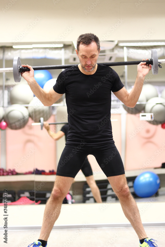 Middle aged man doing wide stance barbell squat in gym Middle aged man doing wide stance barbell squat in gym