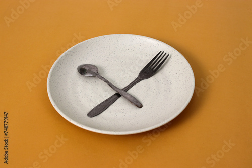 Empty plate with spoon and fork on a yellow background, representing fasting during Ramadan and the anticipation of breaking fast photo