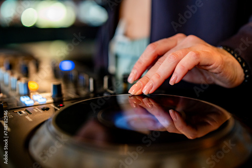 close-up of hands skillfully adjusting knobs and sliders on a professional DJ mixer, illuminated by colorful lights. The mood conveys focus and control during a live music event