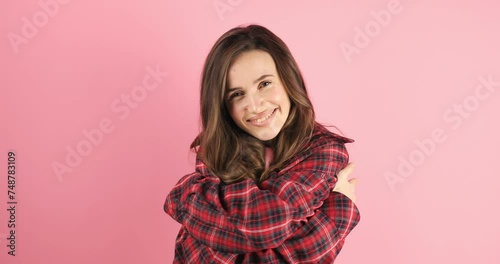Come into my arms. Adorable happy girl with brown hair in plaid shirt gesturing come here for free hugs and smiling sincerely with welcoming expression isolated on pink background. Come to me! photo