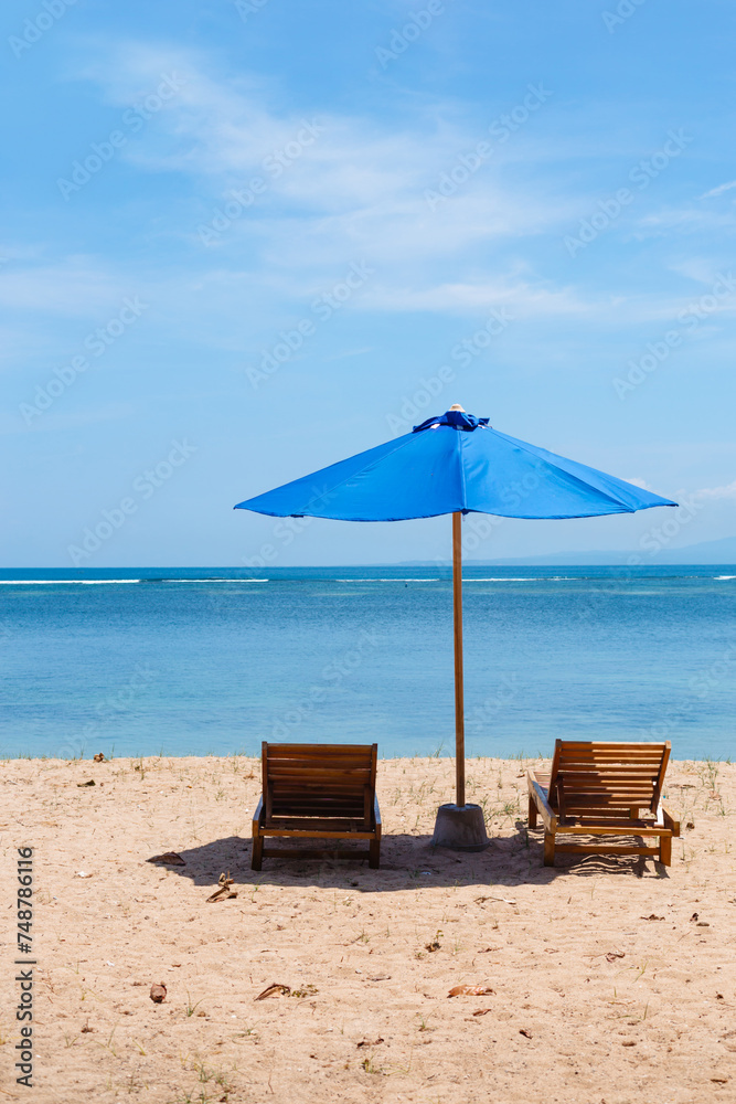 Sunbeds and a blue umbrella against the background of the sea. Concept of relaxing on the beach