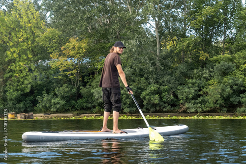 Man exercises while standing on SUP board on water. Sporty man enjoys active weekends in countryside engaging in water sports on lake