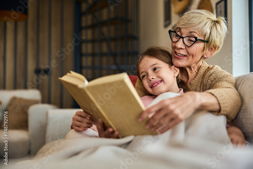 A lovely grandma reading a book story for her grandchild, sitting on the couch, wrapped in a blanket.