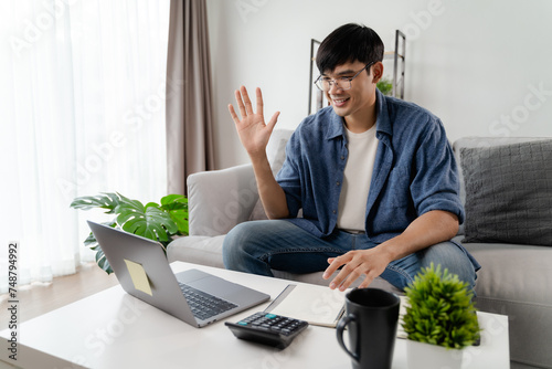  the man in casual clothes working with a laptop, computer, smart phone, calculator sitting on the sofa in the living room at home, working from home concept.